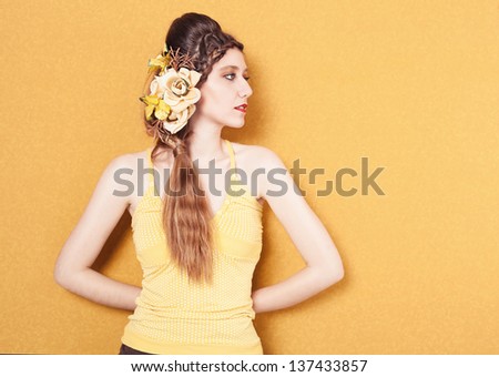 profile portrait of young beautiful lady with flowers on her braided hair on yellow background