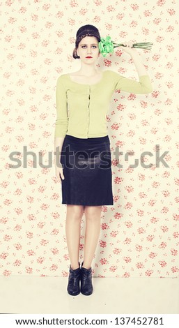 serious retro lady holding flowers like a gun posing in front of a flowered wall background