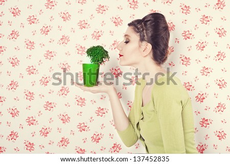 retro style lady smelling a basil plant in a flowerpot in front of red flowered retro wall background