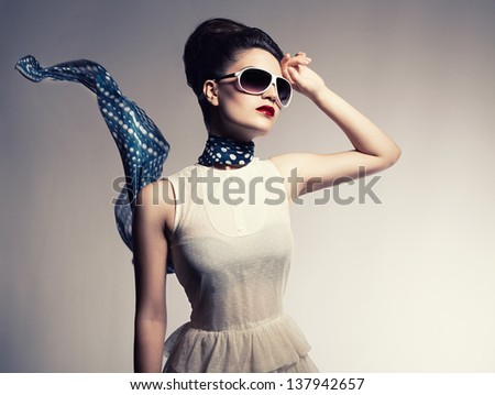 young beautiful fashion model with a flying scarf and sunglasses posing on gray background