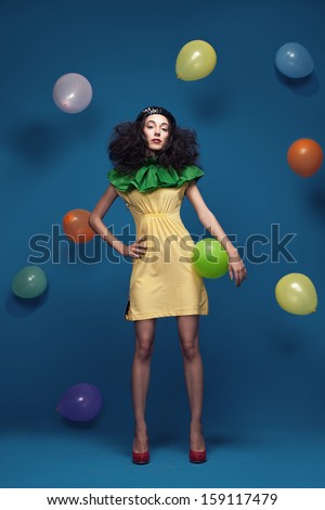 young lady with colorful clothes posing on blue background with flying balloons around