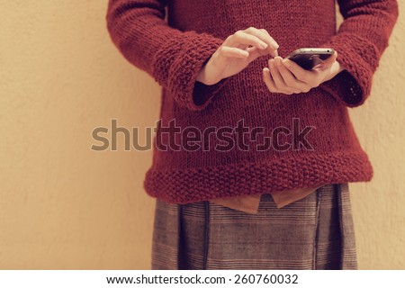 filtered photo of an young woman holding a smart phone and touching the screen with her finger