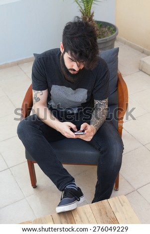 young guy with beard and tattooed arm using a smartphone