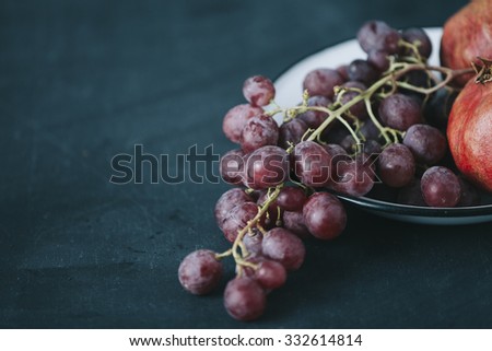 fresh grapes and pomegranate in old vintage plate, on dark blue colored table