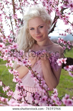 portrait of young cheerful pretty blond woman wearing pink dress in  blooming peach garden