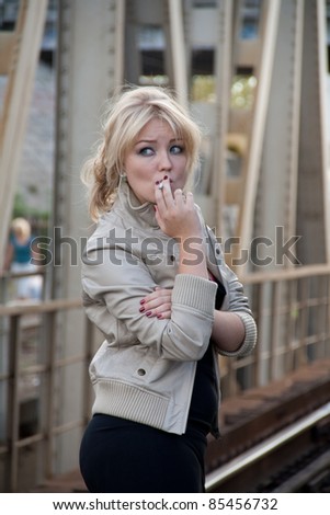 portrait of beautiful blond woman standing on the bridge and smoking