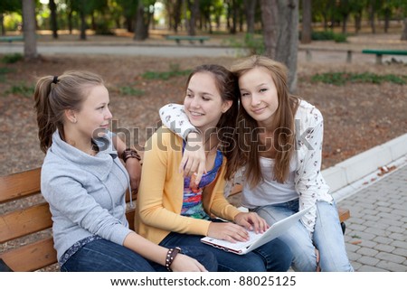 Portrait of three pretty student girls in the park surfing the internet