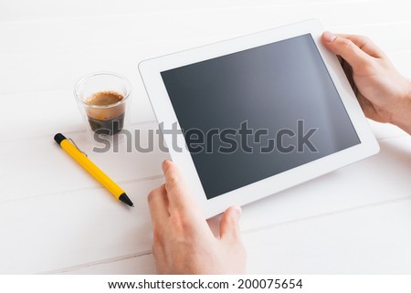 Hands of a man holding blank tablet device over a white wooden workspace table