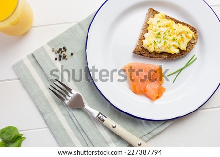 Top view of healthy breakfast with scrambled eggs on toast, smoked salmon, fresh orange juice and green salad