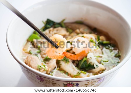 Hand hold shrimp with chopsticks of thai style spicy noodles soup