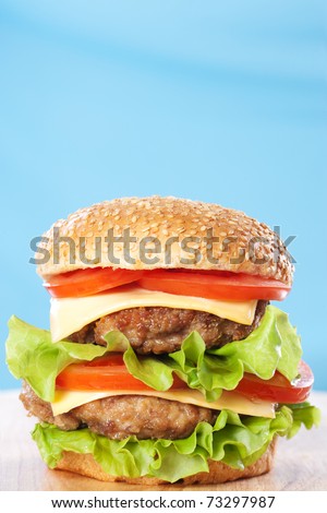 Double cheeseburger with tomatoes and lettuce on blue background