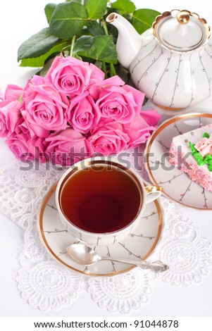 Closeup of cup of tea with cake and roses
