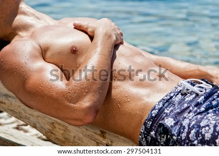Muscular young athletic sexy man lying on the beach with a naked torso in underwear