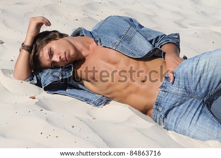 Muscle sexy wet naked young boy lying on the sands in jeans clothes