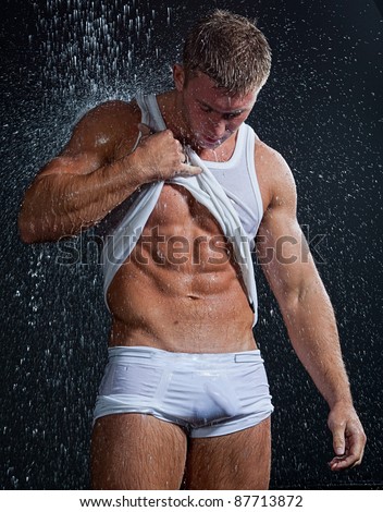 Muscle wet sexy young man takes off clothes under the rain in studio