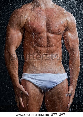 Muscle wet sexy man torso in white shorts posing under the rain in studio