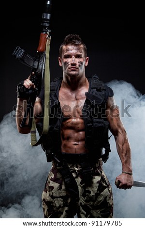 Muscular young sexy naked soldiers with knives and weapons in army clothes in the smoke