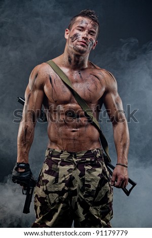 Muscular young wet sexy naked soldiers with weapons in army clothes in the smoke and camouflage paint