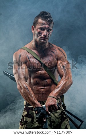 Muscular young sexy naked dirty soldiers with weapons in army clothes in the smoke