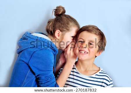 Teenage girl is whispering into the ear of younger boy