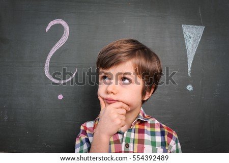 young male caucasian pupil is puzzled in front of a blackboard with question mark and exclamation mark