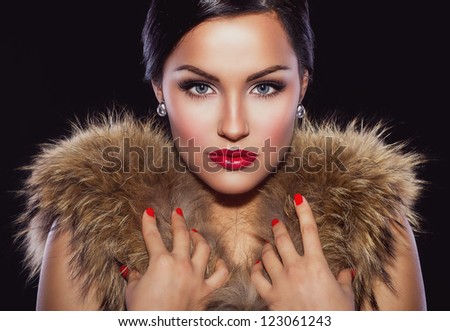 Portrait of a beautiful brunette with classic make up and red lips, holding her hands on fur