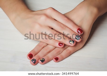 Red nail art with printed flowers on light wooden background