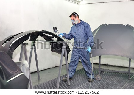 Worker painting car parts in a paint booth.