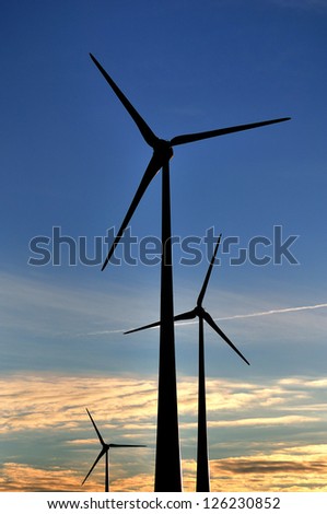 Three wind generators  silhouettes against dark blue sky.