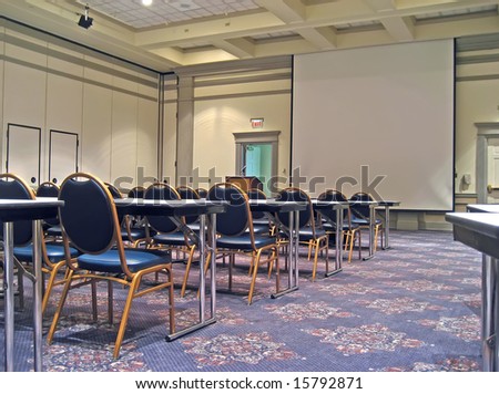 Empty hotel conference room with tables, chairs and projection screen.