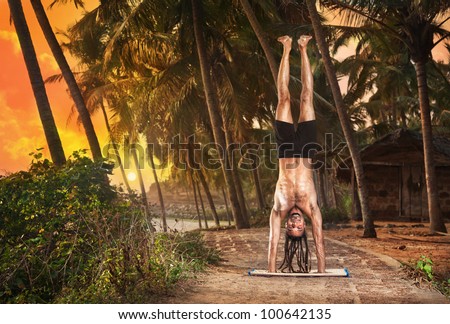 Yoga Adho Mukha Vrksasana handstand pose by fit man with dreadlocks on the beach near the fishermen hut in Varkala, Kerala, India