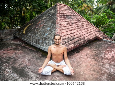 Yoga meditation in lotus pose by man in white trousers on the roof in Varkala, Kerala, India