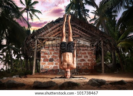 Yoga niralamba shirshasana, head stand pose without hands by fit man with dreadlocks on the beach near the fishermen hut in Varkala, Kerala, India