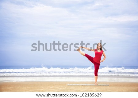 Yoga utthita Hasta Padangustasana one leg balance pose by young woman with long hair in red cloth on the beach at ocean background