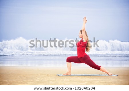 Yoga virabhadrasana I warrior pose by young woman with long hair in red cloth on the beach at ocean background