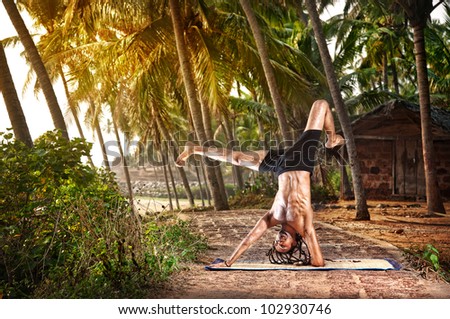 Yoga handstand pose by fit man with dreadlocks on the beach near the fishermen hut in Varkala, Kerala, India