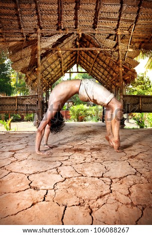 Yoga chakrasana wheel pose by fit man in white trousers on the drought earth in yoga shala, Varkala, Kerala, India