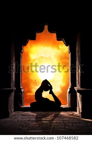 Yoga raja kapotasana pigeon pose by man silhouette in old temple at dramatic sunset sky background. Free space for text