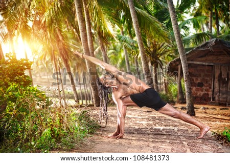 Yoga Parivrtta Parsvakonasana horizon pose by fit man with dreadlocks on the beach near the fishermen hut in Varkala, Kerala, India