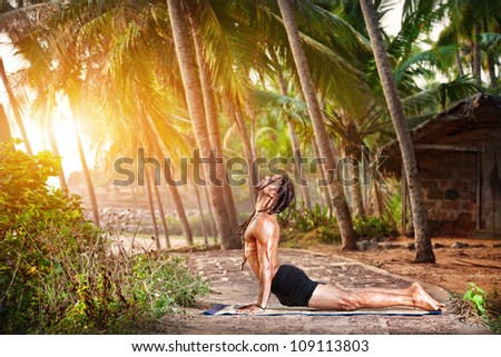 Yoga urdhva mukha svanasana upward facing dog pose by fit man with dreadlocks on the beach near the fishermen hut in Varkala, Kerala, India