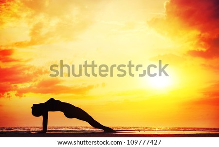 Yoga purvottasana upward plank pose by beautiful woman on the beach near the ocean at dramatic sunset background