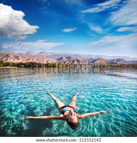 Woman laying like a star in Issyk Kul lake at mountains background in Kyrgyzstan, central Asia