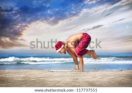 Christmas yoga bakasana crane pose by man in red trousers and Christmas hat on the beach near the ocean in India