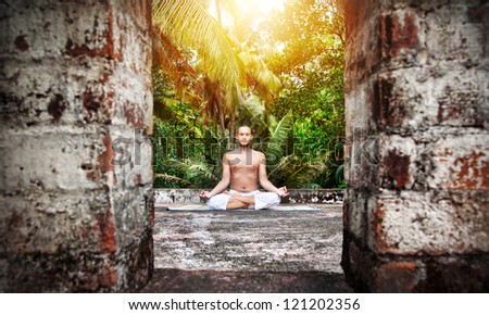 Yoga meditation by man with beard in white trousers on the roof at palms and sunset sky background in India Yoga meditation by man with beard in white trousers on the roof at palms and sunset sky background in India