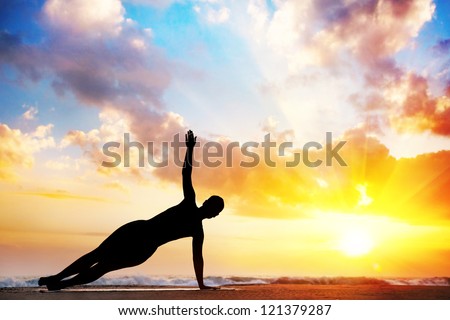 Yoga vasisthasana, side plank pose by woman in silhouette with sunset sky background. Free space for text