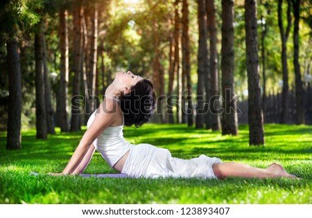 Yoga bhujangasana cobra pose by woman in white costume on green grass in the park around pine trees Yoga bhujangasana cobra pose by woman in white costume on green grass in the park around pine trees