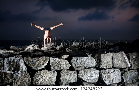 Yoga handstand pose by fit man with dreadlocks on the rocks near the ocean in Varkala, Kerala, India
