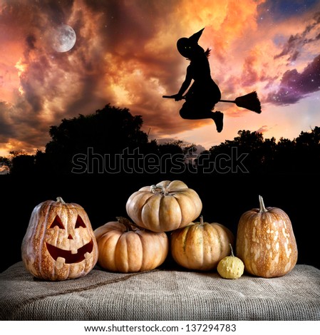 Halloween pumpkins on the table and witch silhouette flying at dramatic night sky with moon
