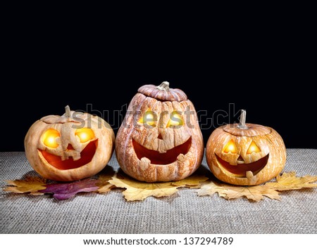 Funny Halloween pumpkins with eyes glowing inside on the dry leaves at black background