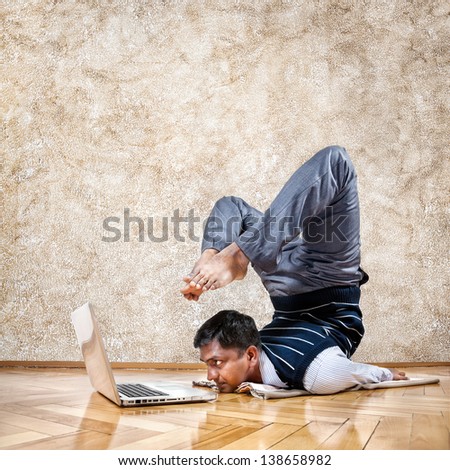Indian businessman doing yoga and looking at laptop in the office at brown textured background